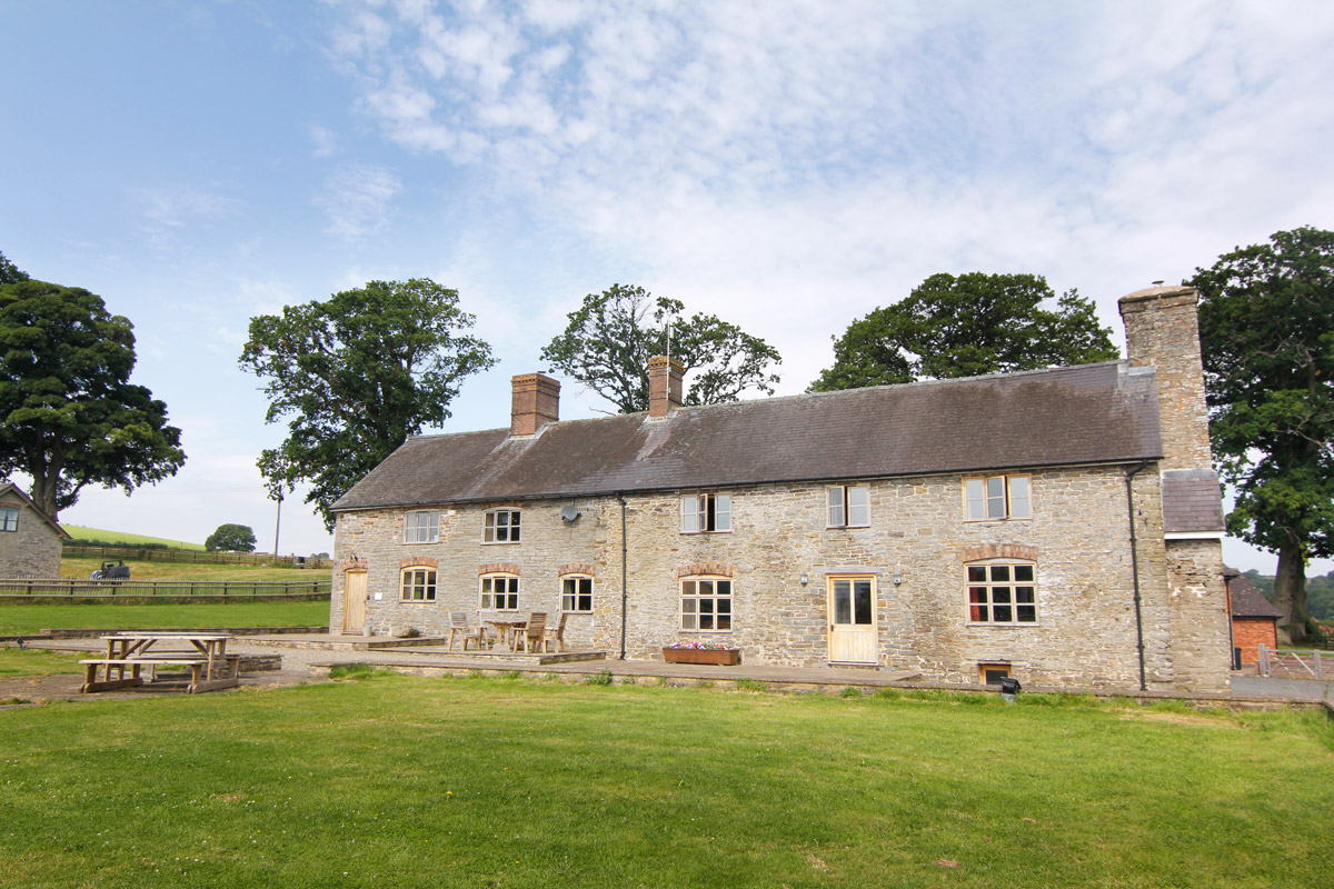 Farmhouse Exterior: “Charming view of Colstey Farmhouse’s rustic exterior, surrounded by lush greenery and scenic countryside.”